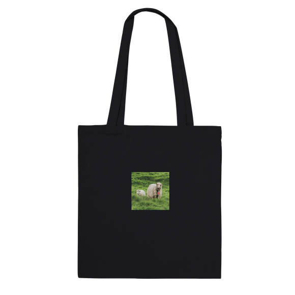 Black tote bag featuring a centered print of a sheep and lamb in lush green grass.