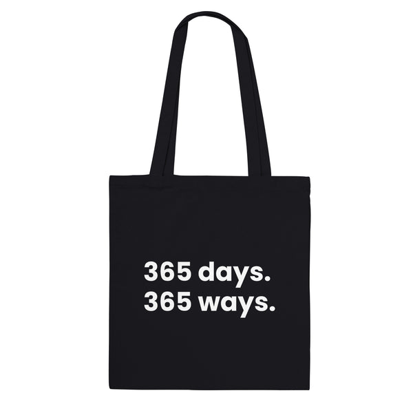 A black canvas tote bag designed by North Minimal featuring white letter text that reads "365 days. 365 ways.". The image shows the front of the tote bag with the text centered and clearly visible on the black background.