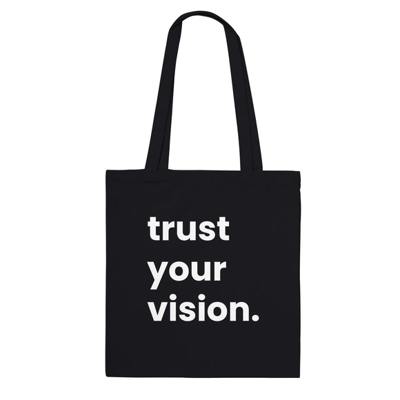 A black canvas tote bag designed by North Minimal featuring white letter text that reads "trust your vision". The image shows the front of the tote bag with the text centered and clearly visible on the black background.